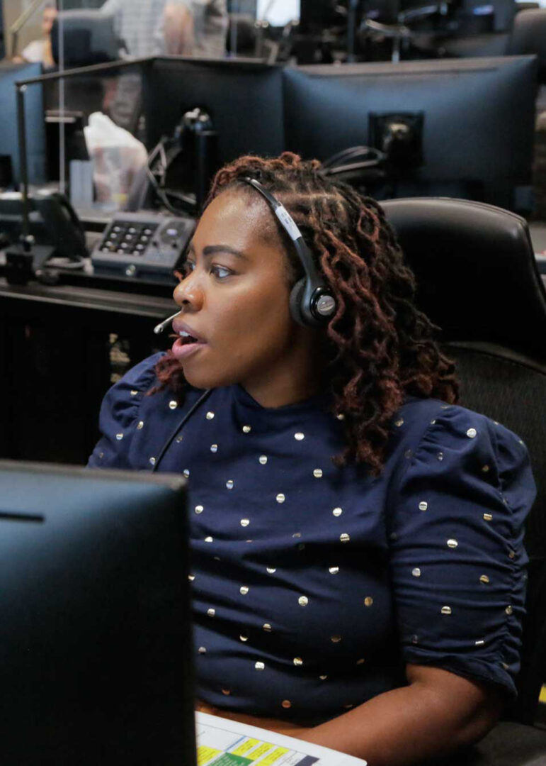 A communications operator is wearing headphones and interacting with a computer.